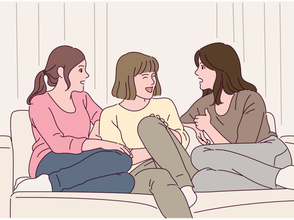 Three female friends sitting on a couch and happily chatting and laughing with each other.